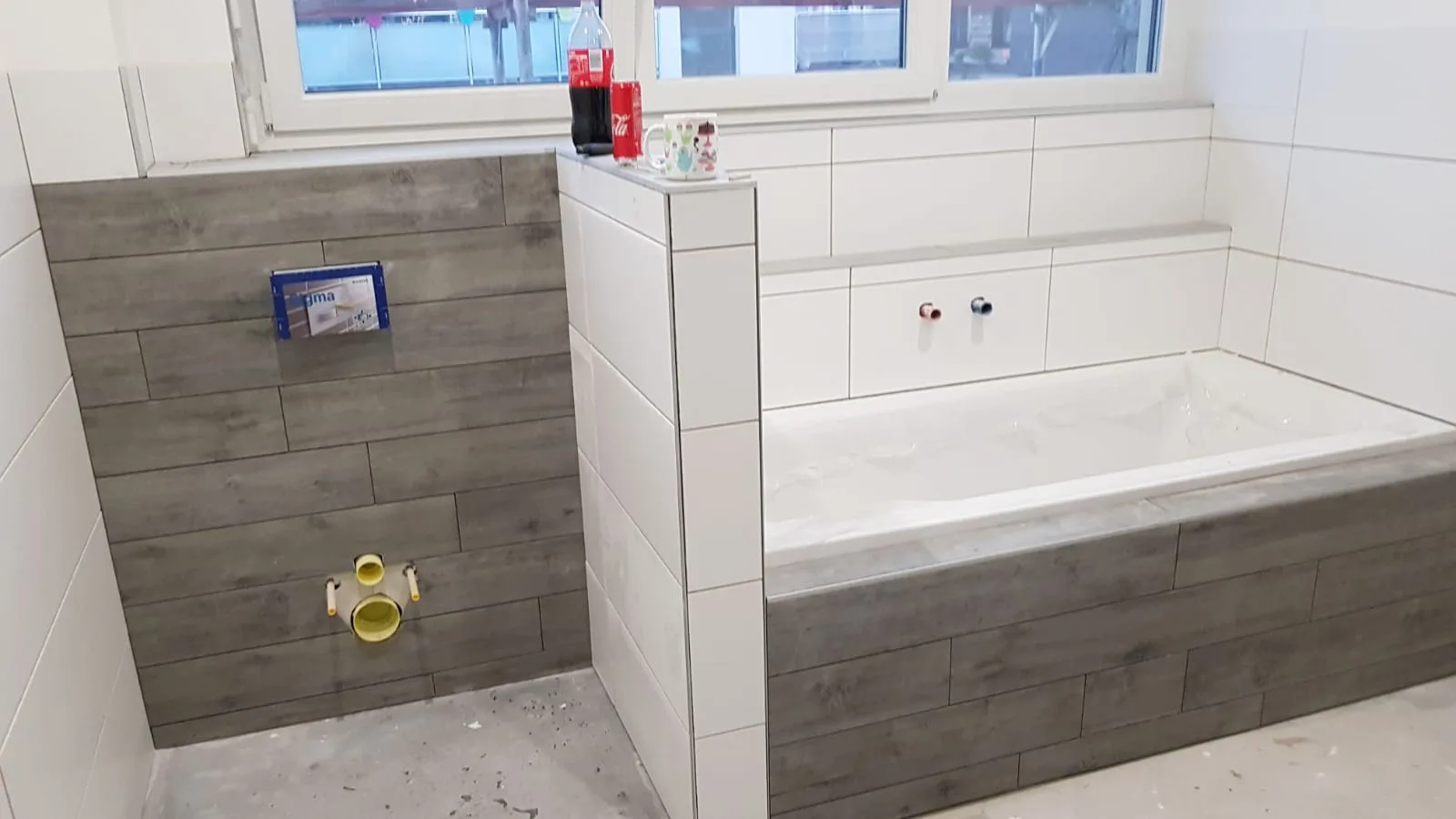 Badewanne vor einer grau gestalteten Fliesenwand